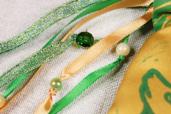 Close Up of Selkie Pouch green and gold ribbons, iridescent green and cream plastic beads and clear green plastic beads