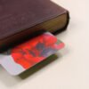 Red poppy flower, Papaver rhoeas, yellow rose, purple pansy painting on bookmark protruding from old hardcover bound book.