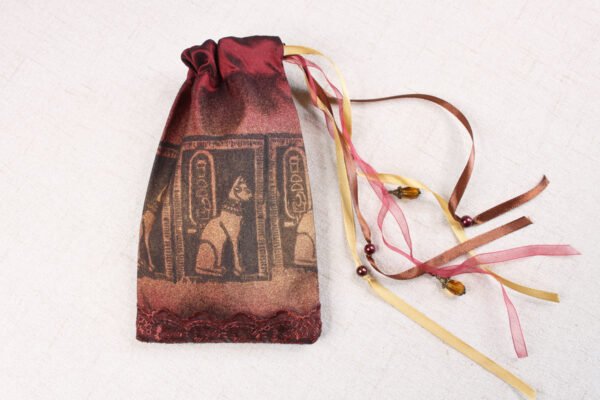 Burgundy handprinted fabric drawstring bag with Cat Goddess print closed with colourful ribbons, charms and beads splayed out