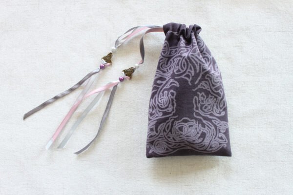 Purple handprinted fabric drawstring bag with spiralling tree print closed with colourful ribbons and beads splayed out