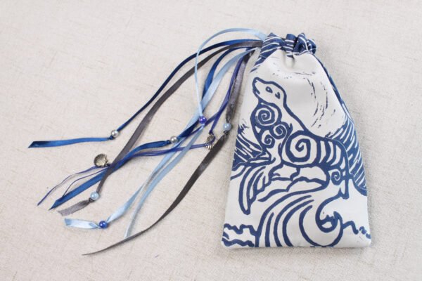 White handprinted fabric drawstring bag with blue spiralling seal print closed with colourful ribbons and beads splayed out