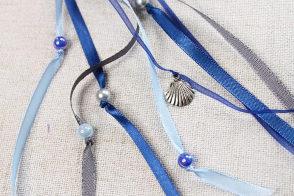 Close Up of Selkie Pouch blue and grey ribbons, iridescent blue and grey plastic beads and silver metal scallop shell charms