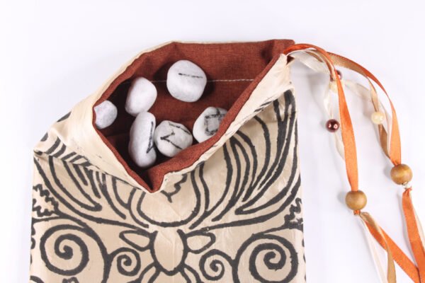 Beige Taffeta Cernunnos pouch with burnt sienna lining, white rune stones that spell Imogen are sitting in the pouch